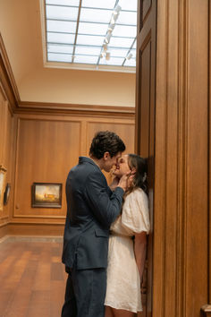 a man and woman kissing each other in front of a wooden wall with paintings on the walls