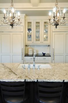 a kitchen with white cabinets and marble counter tops, chandelier above the sink