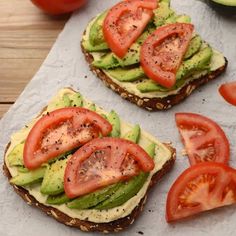 avocado and tomato sandwich on top of a piece of parchment paper next to sliced tomatoes