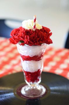 a red and white layered dessert in a tall glass vase with a candle on top