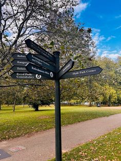 a sign post with many signs on it in the grass next to a path and trees