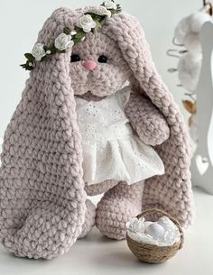 a crocheted bunny sitting next to a basket filled with white eggs and flowers