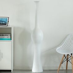 a white vase sitting on top of a table next to a chair