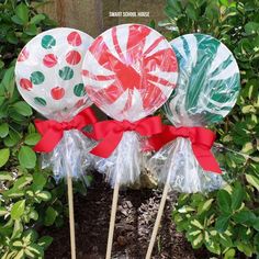 three lollipops wrapped in cellophane and tied with red ribbon are sitting on the ground