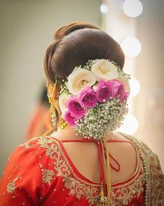 a woman with flowers in her hair wearing a red and gold sari, looking down at the ground