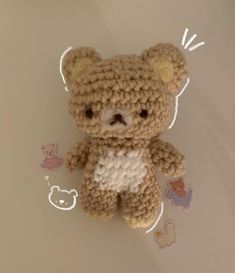 a crocheted teddy bear sitting on top of a white table next to stickers