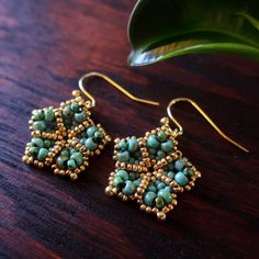 two pairs of earrings on top of a wooden table next to a green potted plant