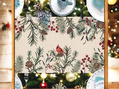 a christmas table setting with plates, silverware and a red cardinal on the tree