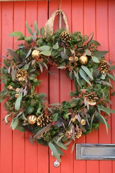 a red door with a wreath hanging from it's side and pine cones on the front