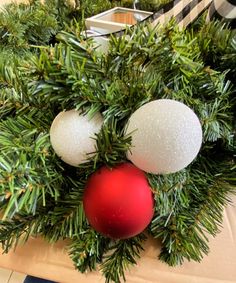 two christmas ornaments are sitting on top of a wreath with pine needles and red ornament balls