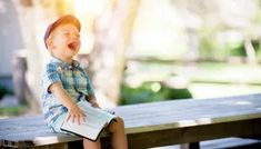 a little boy that is sitting on a bench with a book in his hand and laughing