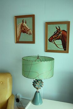 a lamp sitting on top of a white table next to two framed horse pictures above it