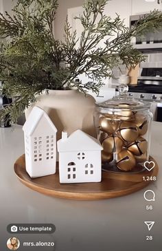 a wooden tray topped with gold and white ornaments next to a vase filled with greenery