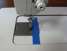 a white sewing machine with blue tape on it's side and the needle pointing up