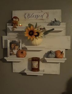 two white shelves with pumpkins and sunflowers on them next to a candle