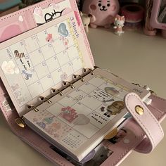 an open pink planner book sitting on top of a table next to a stuffed animal