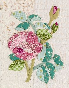 a close up of a flower on a quilted piece of cloth with green leaves and pink flowers