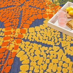 an orange, yellow and blue rug with fruit on it next to a white tray