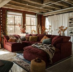 a living room with red couches and pillows on top of the sofa, in front of two windows