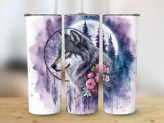 three travel mugs with wolf and dream catcher designs on them sitting on a table