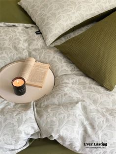 an open book and candle on a bed with white comforter, pillows and pillow cases