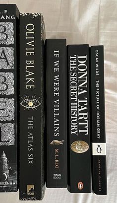 four black books are lined up on a white bed sheet in front of a white comforter