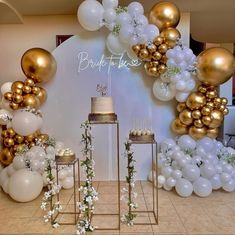 a table topped with cake and balloons in front of a wall covered in white and gold balloons