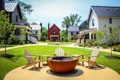 a fire pit surrounded by lawn chairs in front of two houses with landscaping around it