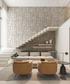 a living room filled with furniture next to a white stair case and wall covered in stone