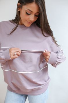 a woman wearing a purple sweater is holding something in one hand and looking down at the other