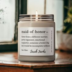 a candle that reads maid of honor on the front and back of it, sitting on a table next to a potted plant