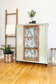 a green cabinet sitting on top of a hard wood floor next to a potted plant