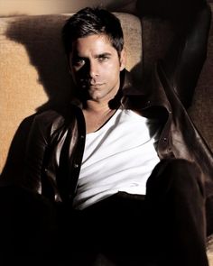 a man sitting on top of a couch next to a brown leather jacket and white t - shirt