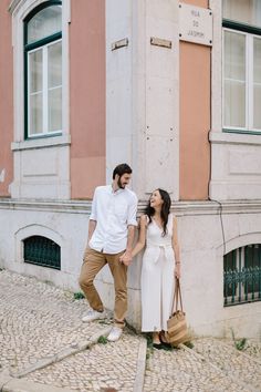 a man and woman standing next to each other in front of a building holding hands