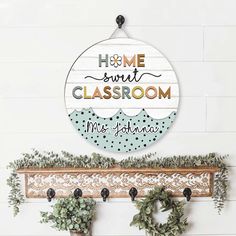 a sign that says home sweet classroom hangs on the wall above two potted plants