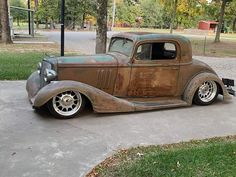 an old, rusted car is parked on the sidewalk in front of some trees