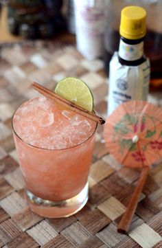 a pink drink with a lime slice on the rim and an orange umbrella next to it