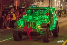 a green jeep driving down a street with christmas lights on it's hood and decorations