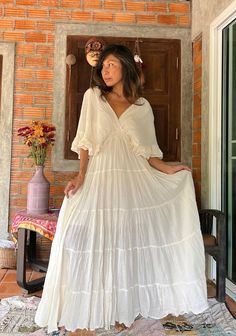 a woman standing in front of a brick wall wearing a white dress with ruffles