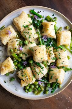 a white plate topped with tofu and asparagus on top of a wooden table