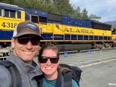 a man and woman taking a selfie in front of a blue and yellow train