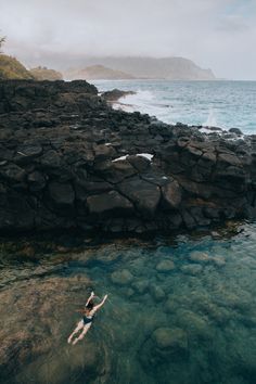 a person swimming in the ocean near some rocks