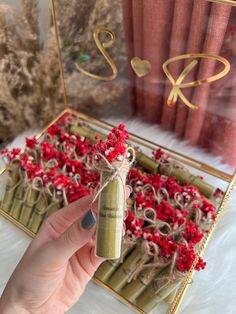 a hand holding a small bottle with red flowers in it next to some bamboo sticks