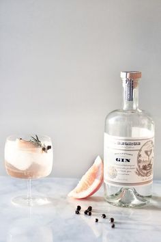 a bottle of gin next to a glass filled with ice and garnishes