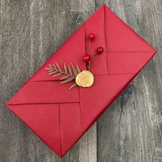 a red envelope with a gold button and some leaves on it sitting on a wooden table