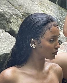 two women sitting next to each other in front of some rocks and water with their faces close together