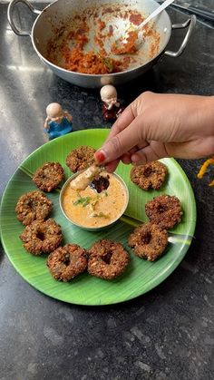 a person dipping some food into a bowl on a green plate next to a pan