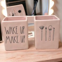 two pink ceramic containers with black writing on them sitting on a wooden table in front of a mirror