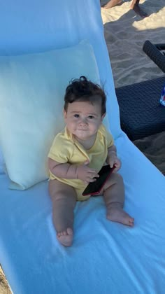 a small child sitting on top of a beach chair with a cell phone in his hand