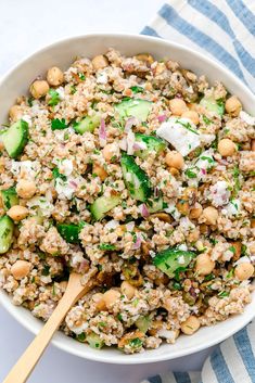 a white bowl filled with rice, cucumber and chickpeas next to a wooden spoon